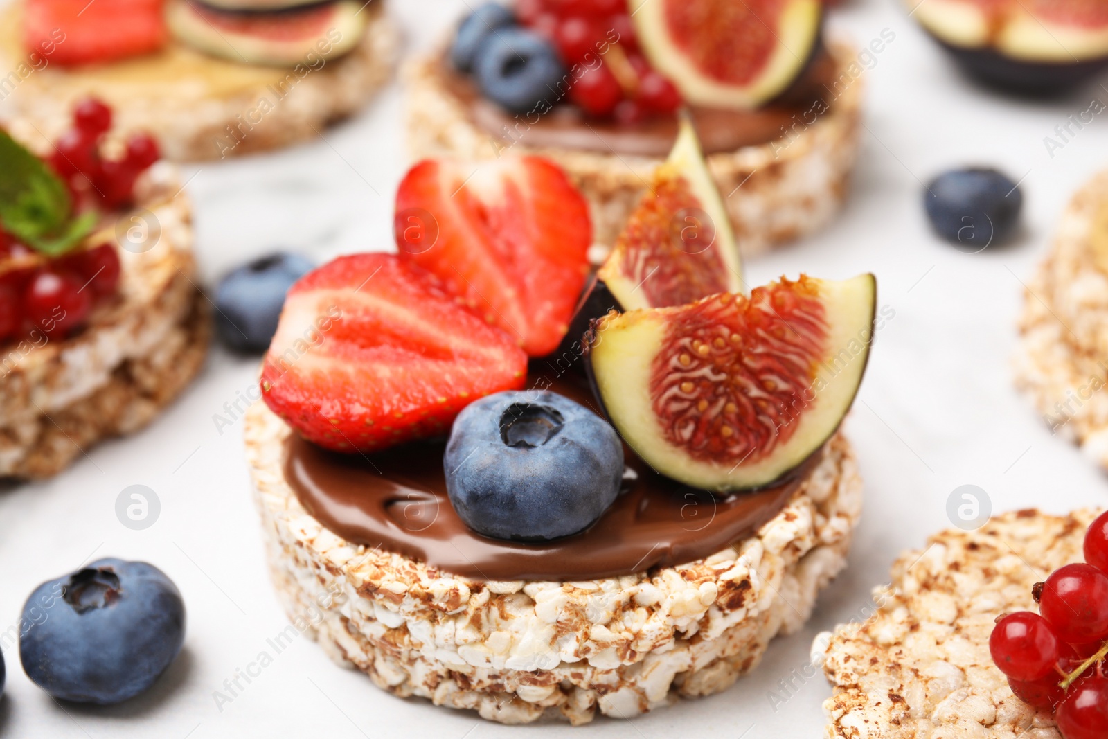 Photo of Tasty crispbreads with chocolate, figs and sweet berries on light table, closeup