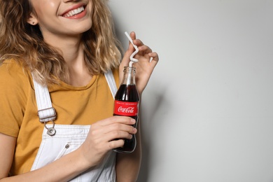 Photo of MYKOLAIV, UKRAINE - NOVEMBER 28, 2018: Young woman with bottle of Coca-Cola on white background, closeup. Space for text