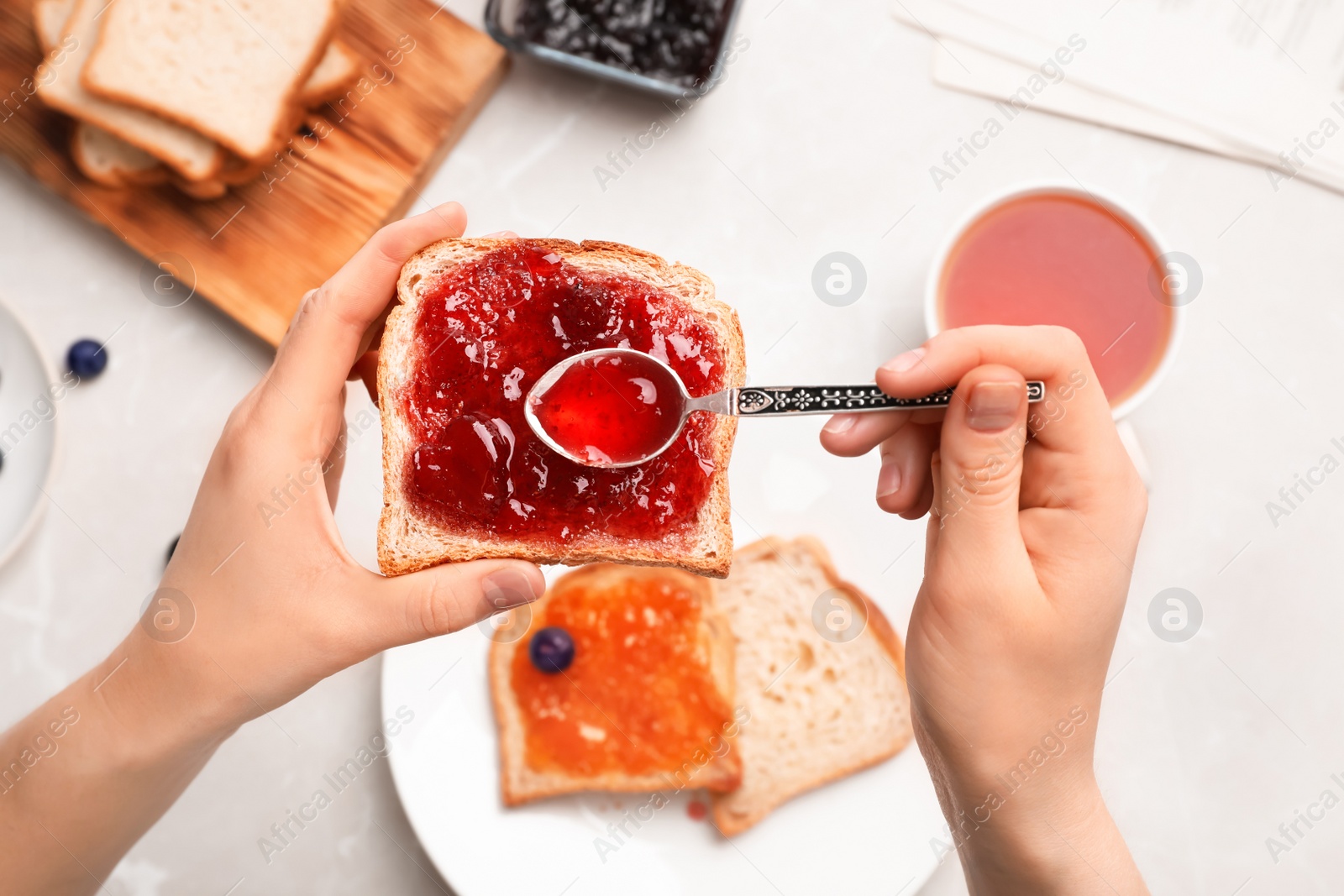 Photo of Woman spreading jam on toast over table