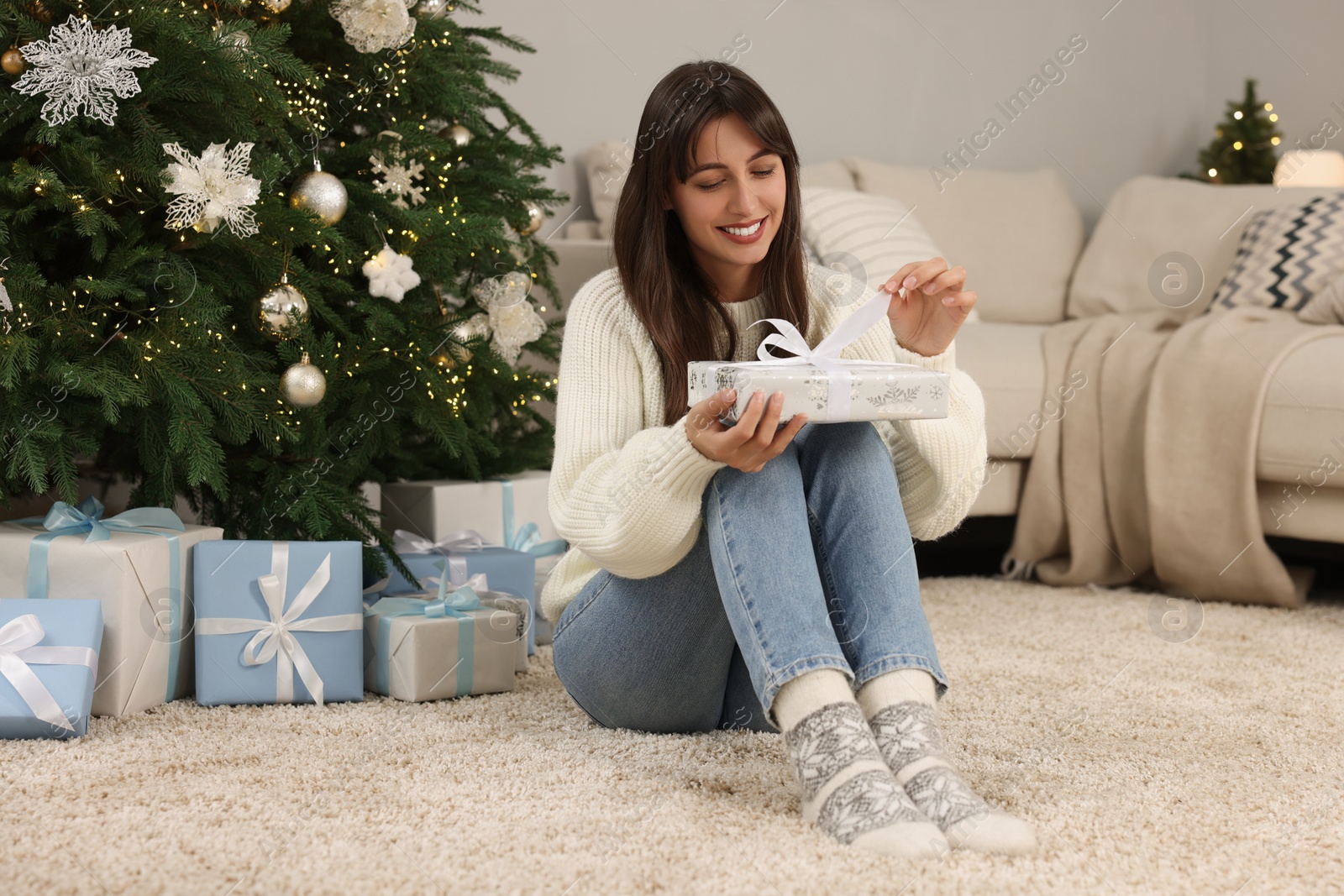 Photo of Smiling woman opening Christmas gift at home