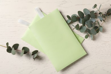 Scented sachets and eucalyptus branches on white wooden table, flat lay