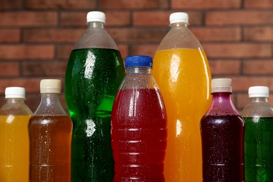 Photo of Bottles of soft drinks with water drops near brick wall, closeup