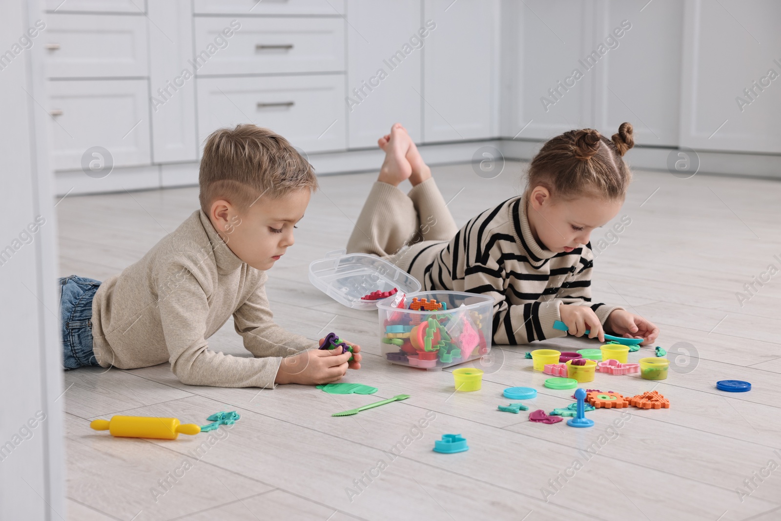 Photo of Cute little children playing together on warm floor in kitchen. Heating system