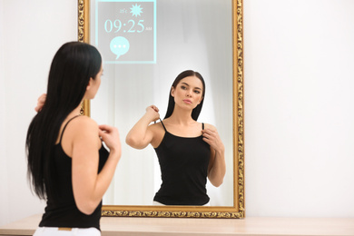 Beautiful young woman looking at herself in smart mirror indoors