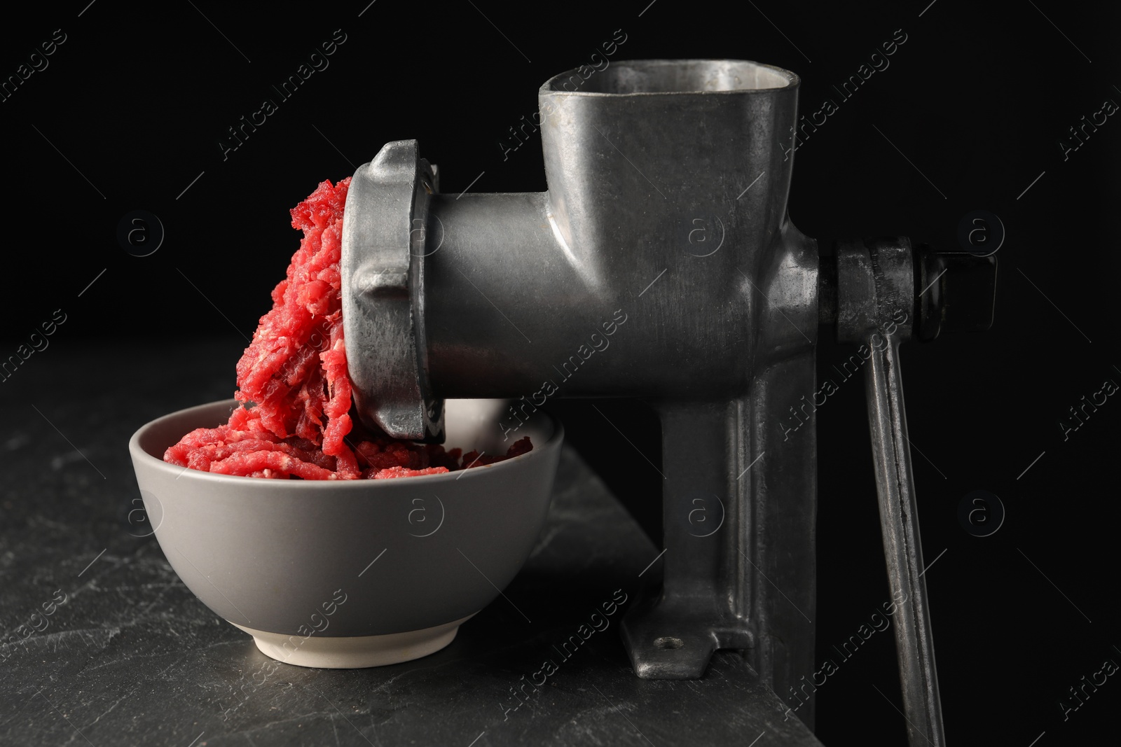 Photo of Metal meat grinder with beef mince on dark textured table against black background