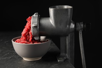 Metal meat grinder with beef mince on dark textured table against black background