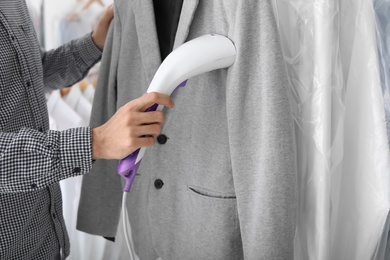 Young man steaming jacket at dry-cleaner's