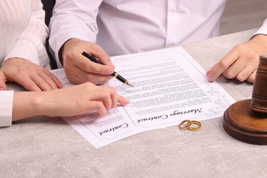 Man and woman signing marriage contract at light grey table, closeup