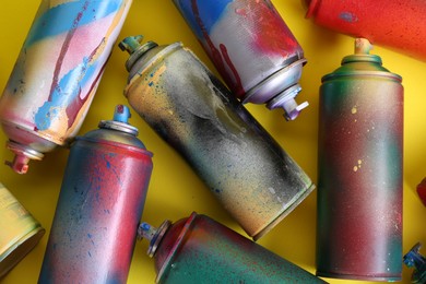 Many spray paint cans on yellow background, flat lay