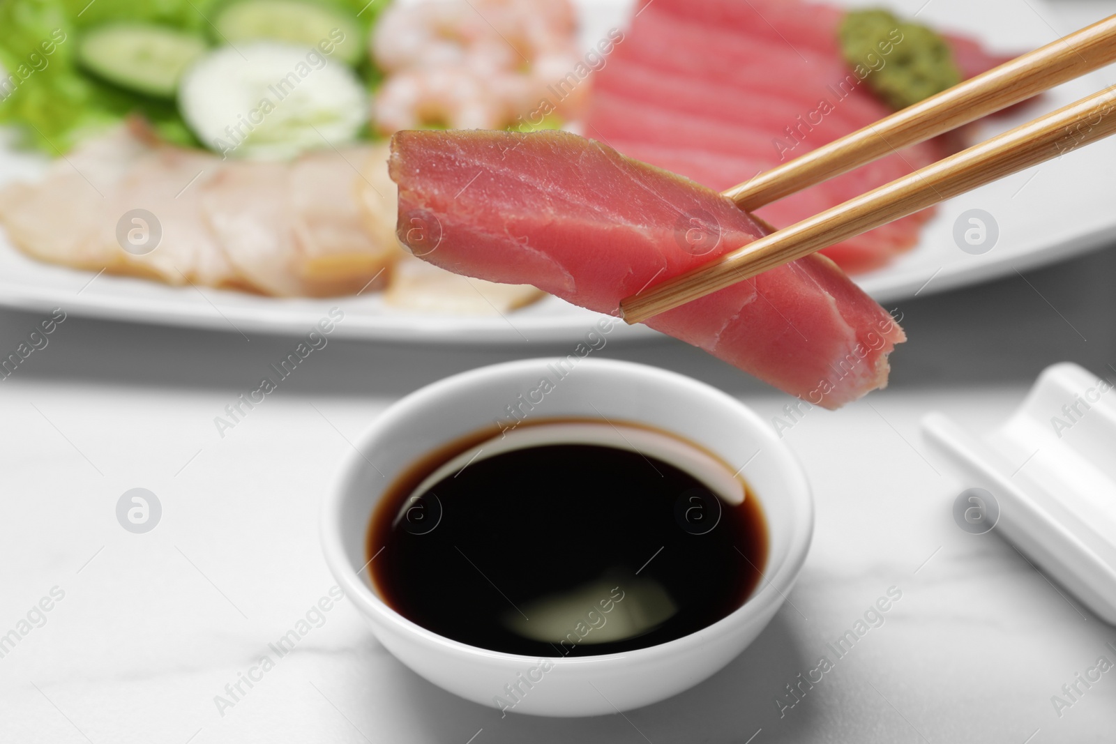 Photo of Chopsticks with raw tuna piece under soy sauce on white table, closeup. Sashimi set