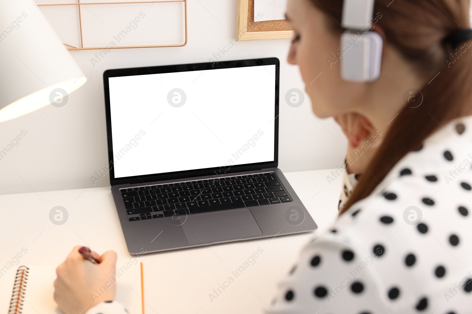 Photo of E-learning. Woman taking notes during online lesson at table indoors, closeup