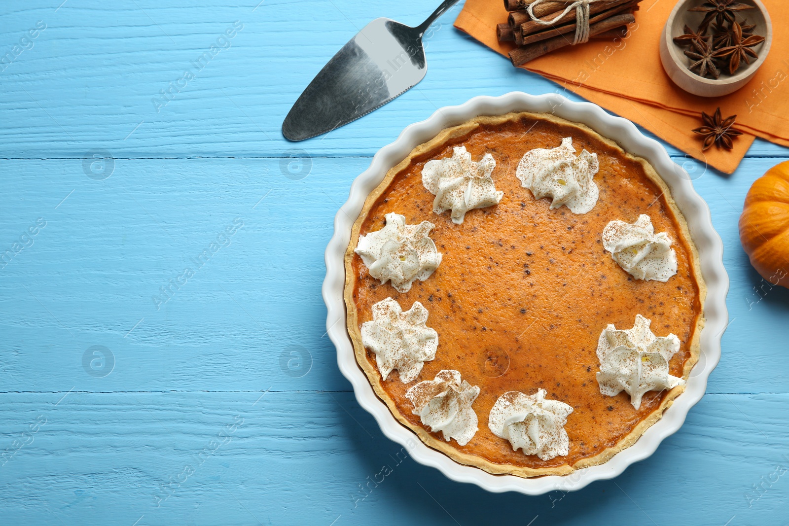 Photo of Delicious pumpkin pie with whipped cream and spices on light blue wooden table, flat lay. Space for text