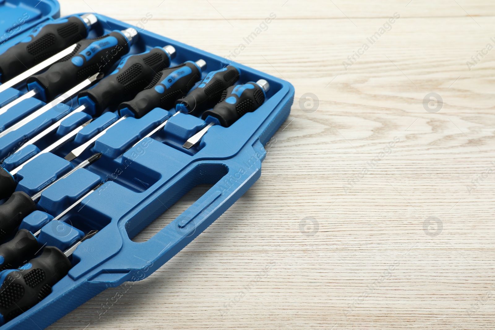 Photo of Set of screwdrivers in open toolbox on light wooden table, closeup. Space for text