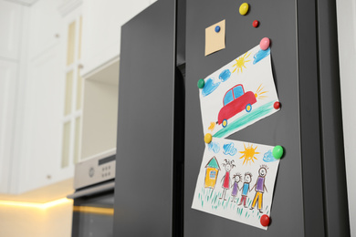 Modern refrigerator with child's drawings and magnets in kitchen