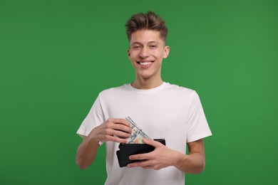 Photo of Happy man putting money into his wallet on green background