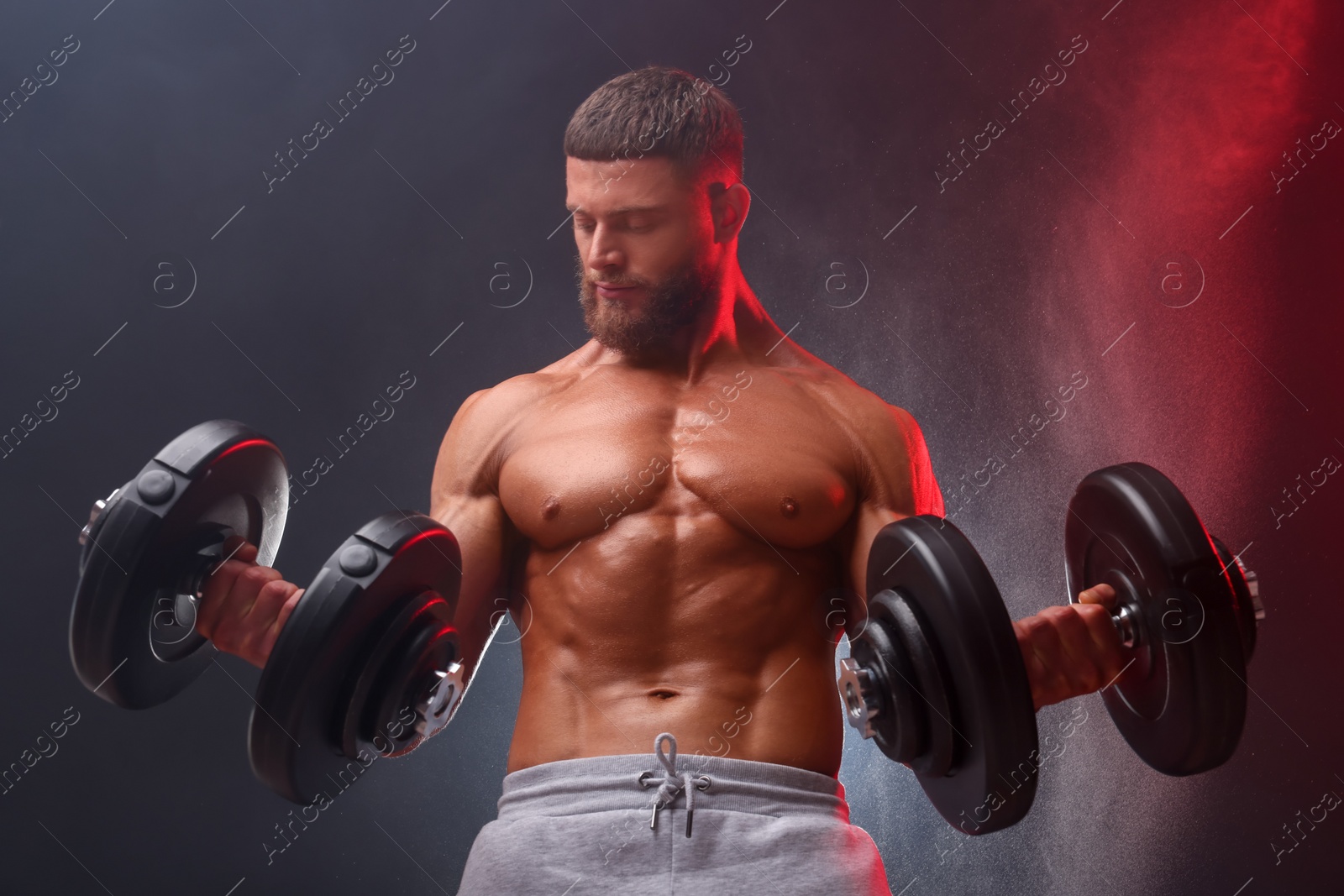 Photo of Young bodybuilder exercising with dumbbells in smoke on color background, low angle view