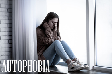 Image of Depressed teenage girl sitting alone near window at home. Autophobia - fear of isolation