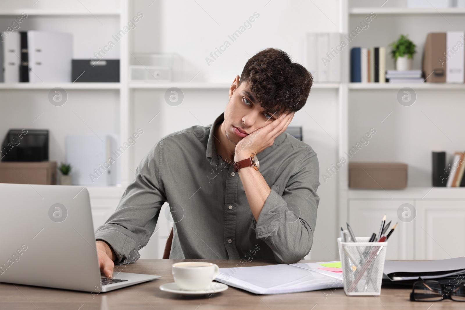 Photo of Tired young man working at table in office. Deadline concept