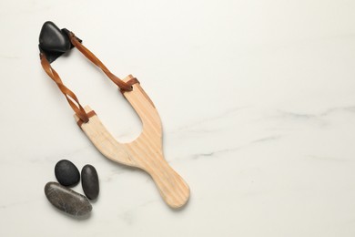 Wooden slingshot with stones on white marble background, flat lay. Space for text