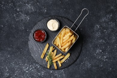Photo of Tasty French fries, ketchup, rosemary and mayonnaise on black textured table, top view