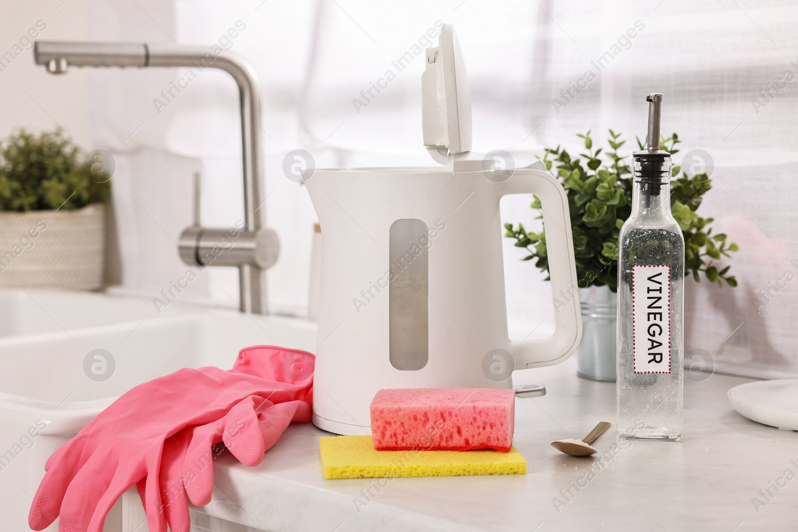 Photo of Cleaning electric kettle. Bottle of vinegar, rubber gloves, sponge and spoon with baking soda on countertop in kitchen