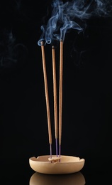 Photo of Incense sticks smoldering in holder on black background