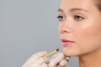 Photo of Young woman getting lips injection on grey background, space for text. Cosmetic surgery