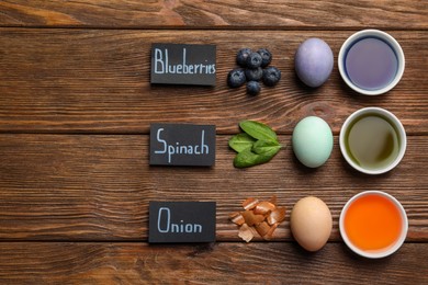 Photo of Easter eggs painted with natural organic dyes, labels and space for text on wooden table, flat lay. Blueberries, spinach, onion used for coloring