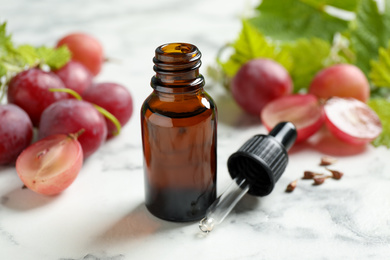 Photo of Bottle of natural grape seed oil on white marble table. Organic cosmetic