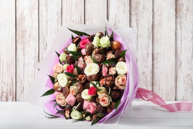 Photo of Beautiful bouquet of flowers and chocolate candies on white wooden table