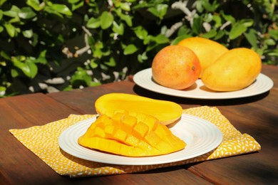 Photo of Plates with tasty mango on wooden table outdoors