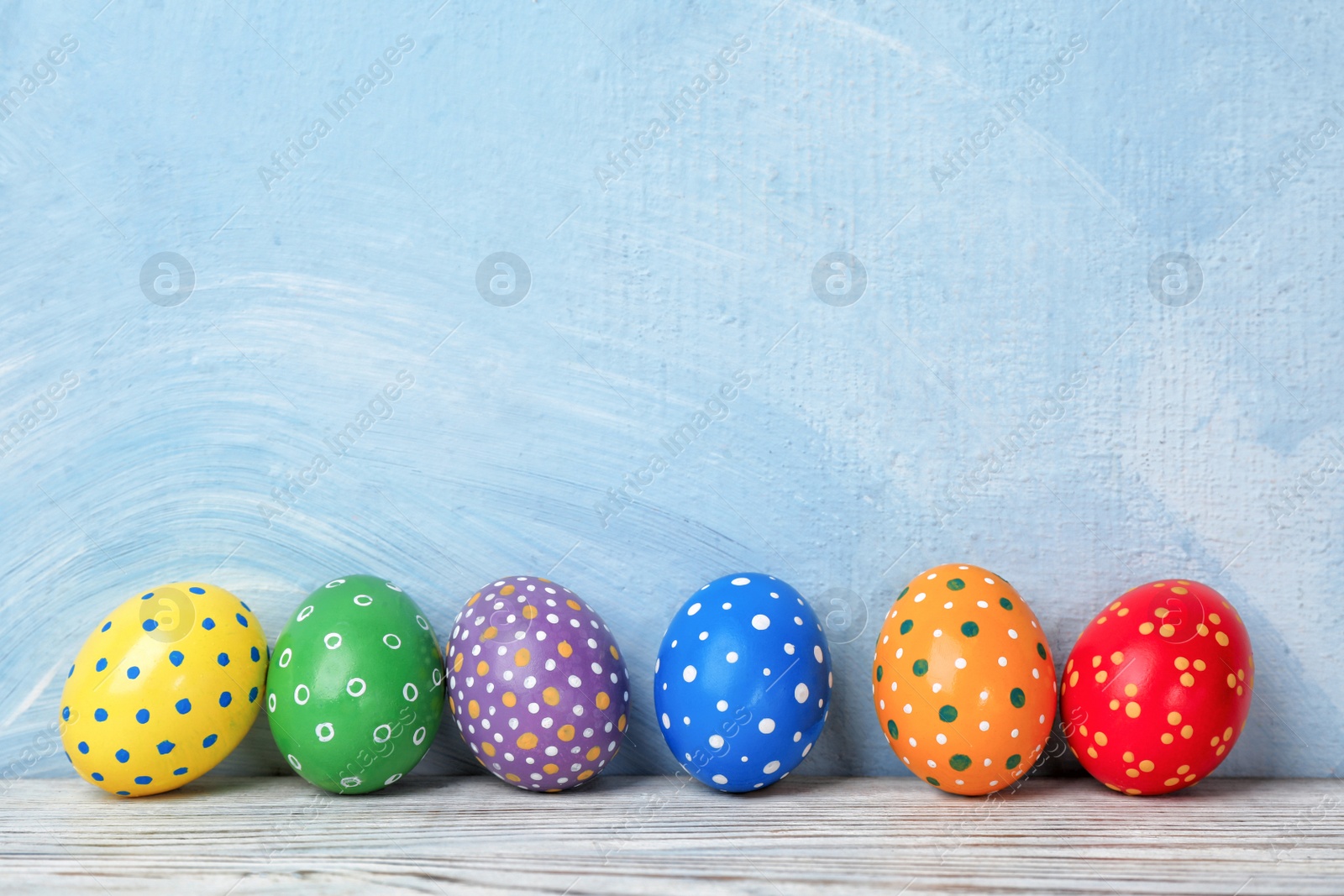 Photo of Decorated Easter eggs on table near color wall. Space for text