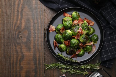 Photo of Delicious roasted Brussels sprouts, bacon and rosemary on wooden table, top view. Space for text