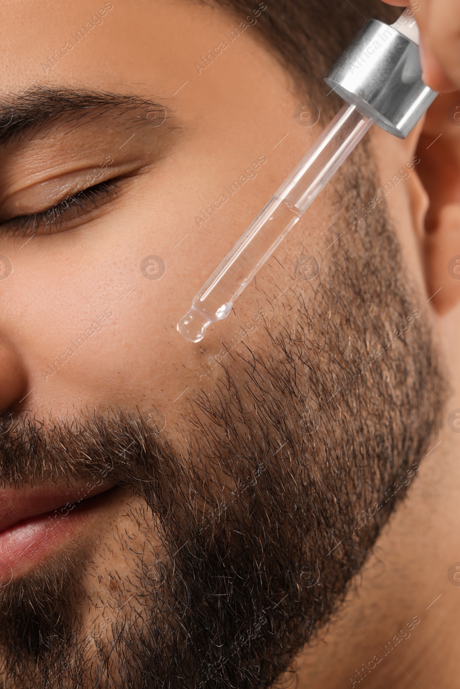 Photo of Man applying cosmetic serum onto face, closeup