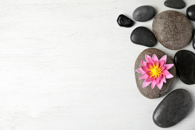 Stones with lotus flower and space for text on white wooden background, flat lay. Zen lifestyle
