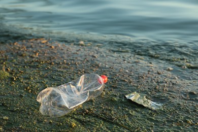 Photo of Used plastic bottle near water at beach, space for text. Environment pollution