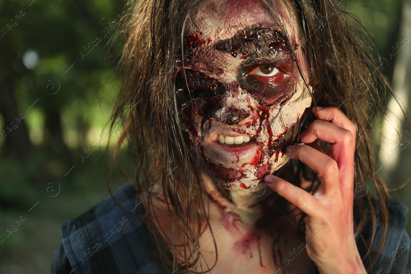 Photo of Scary zombie with bloody face outdoors, closeup. Halloween monster