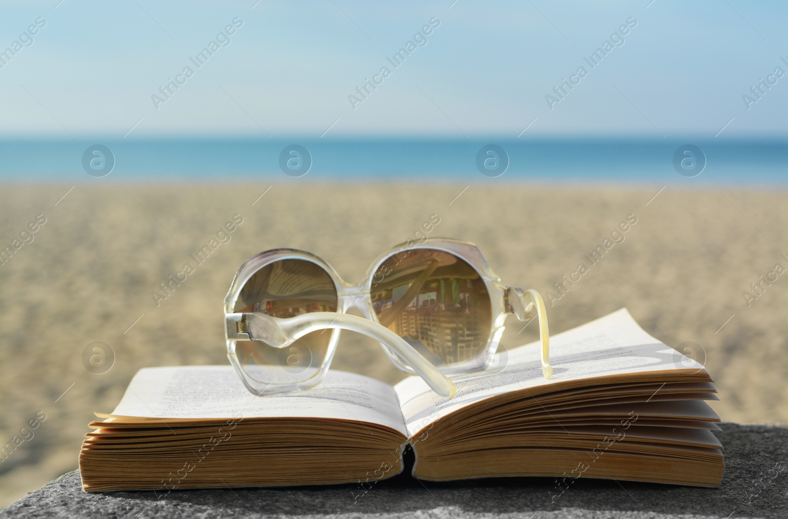 Photo of Book and sunglasses on table at seaside, space for text