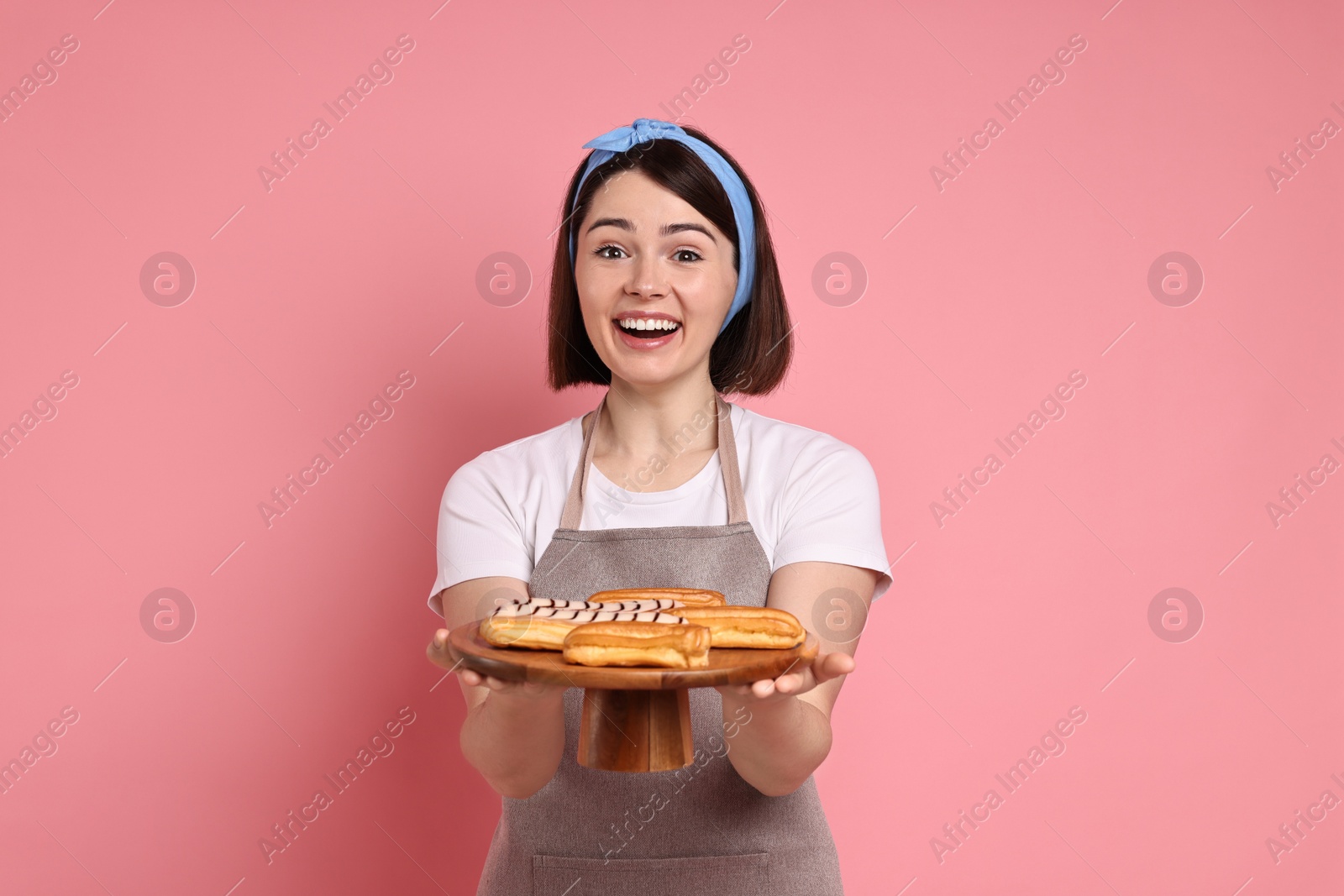 Photo of Happy confectioner with delicious eclairs on pink background