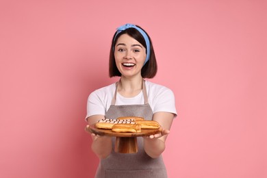 Happy confectioner with delicious eclairs on pink background