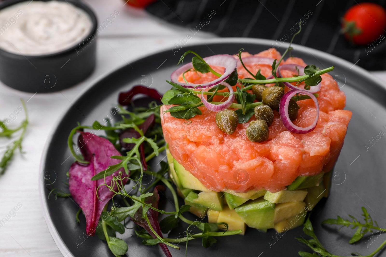 Photo of Tasty salmon tartare with avocado and greens on white table, closeup