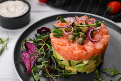 Photo of Tasty salmon tartare with avocado and greens on white table, closeup