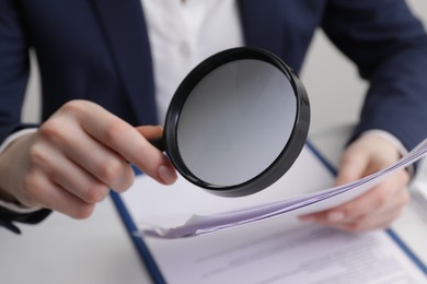 Woman looking at document through magnifier at table, closeup. Searching concept