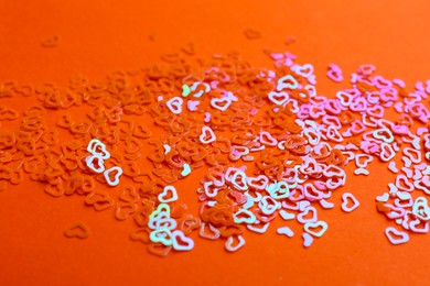 Photo of Shiny bright heart shaped glitter on coral background, closeup
