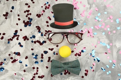 Photo of Clown face made of mask, cylinder and bow tie on light grey stone table, flat lay
