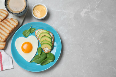 Photo of Romantic breakfast with heart shaped fried egg served on light grey table, flat lay. Space for text