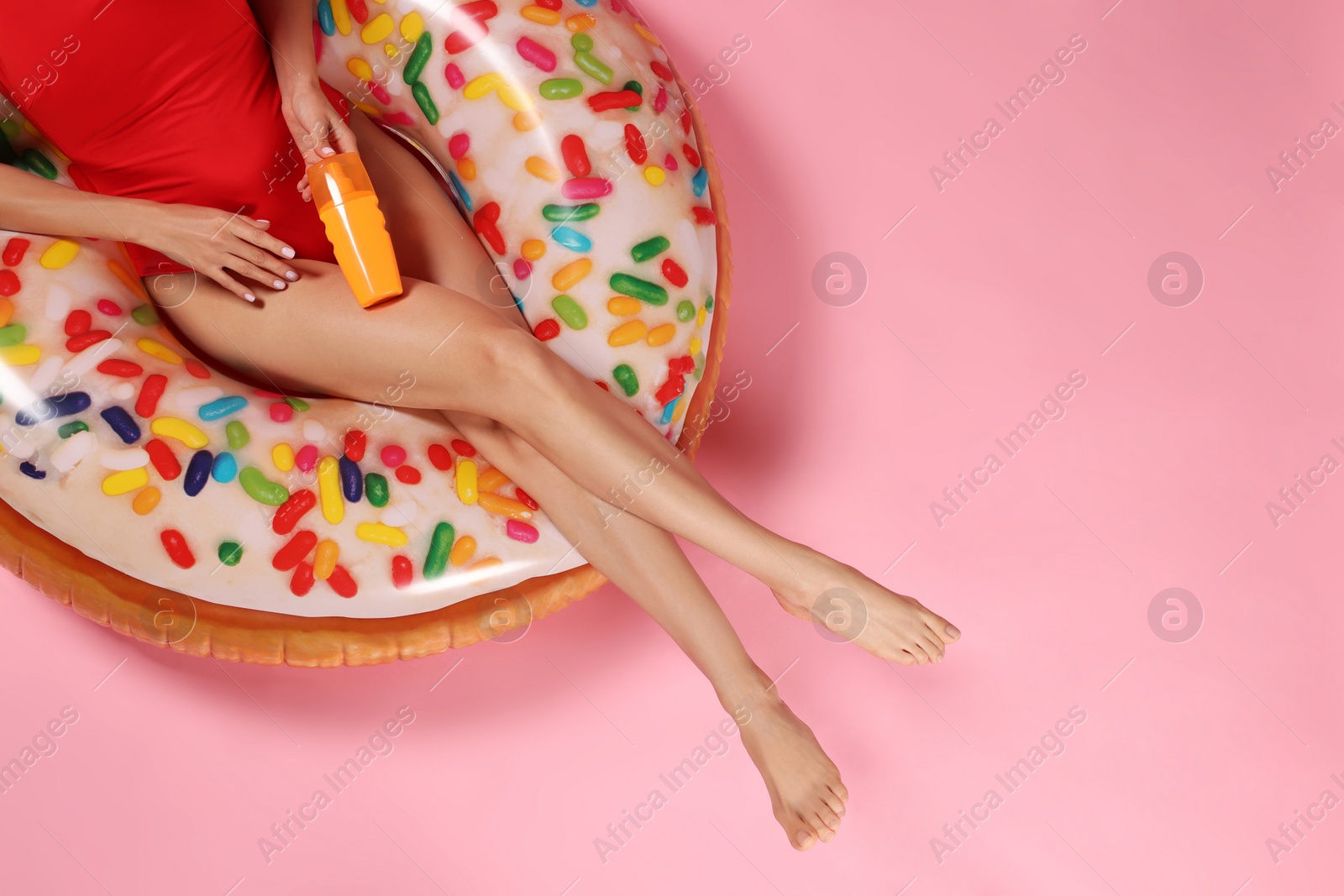Photo of Young woman with sun protection cream on inflatable ring against pink background, closeup. Space for text