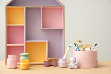 Photo of Composition with house shaped shelf and jars of paints on table. Interior element