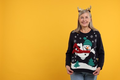Photo of Happy senior woman in deer headband showing Christmas sweater on orange background. Space for text