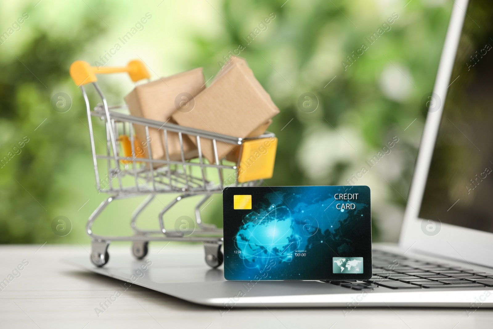 Photo of Online payment concept. Small shopping cart with bank card, boxes and laptop on white table